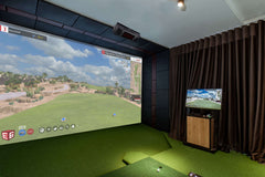 Indoor golf simulator setup with large screen and additional TV.
